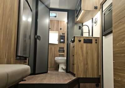 The interior of a CORE RV toy hauler featuring custom cabinetry. Showing the kitchenette with sink, 2 burner cooktop, convection microwave and refrigerator.