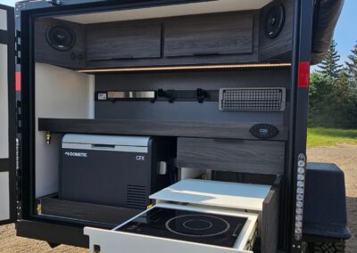 View of CORE RV 5510 galley with dual slide out propane cooktop, fridge slide with dometic 12v fridge, water access, spice rack, paper towlel holder and magnet bar on the back CORE Rail, under cabinet lighting and upper cabinets with bluetooth speakers on both sides