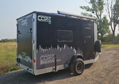 Exterior view of the CORE RV 6515 Trailhead curbside with grey tree graphics and awning on the roof